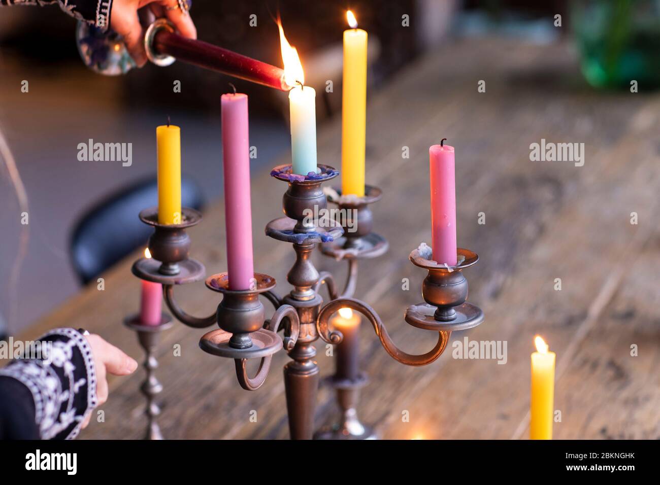 A woman lighting different colored candles in a vintage metal candle holder to create a nice atmosphere in her home. An Eclectic styled living with a Stock Photo