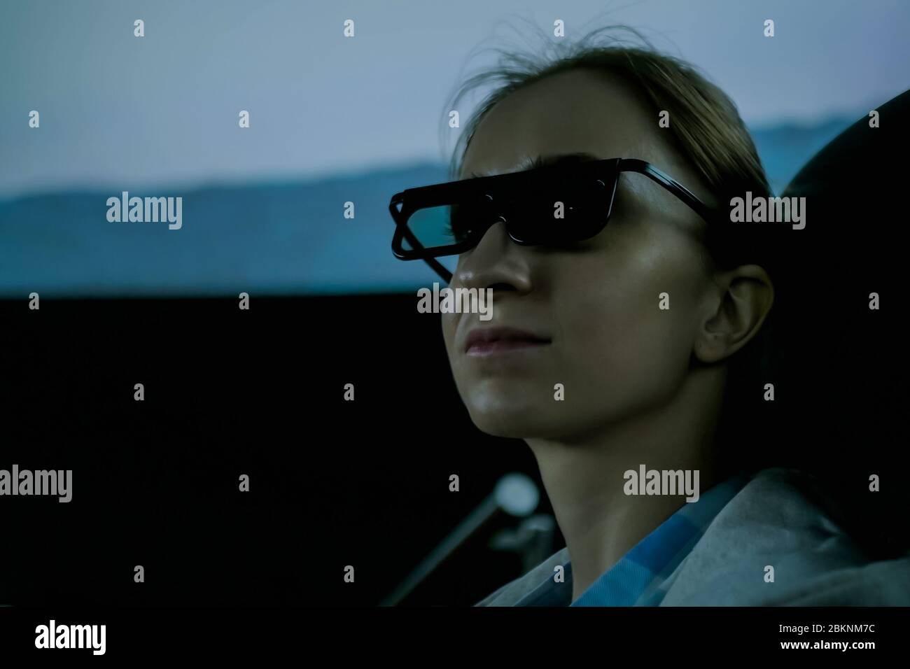 Portrait of woman face with black 3d glasses looking around in movie theater with panoramic screen and low light illumination. Technology, 3d movie Stock Photo