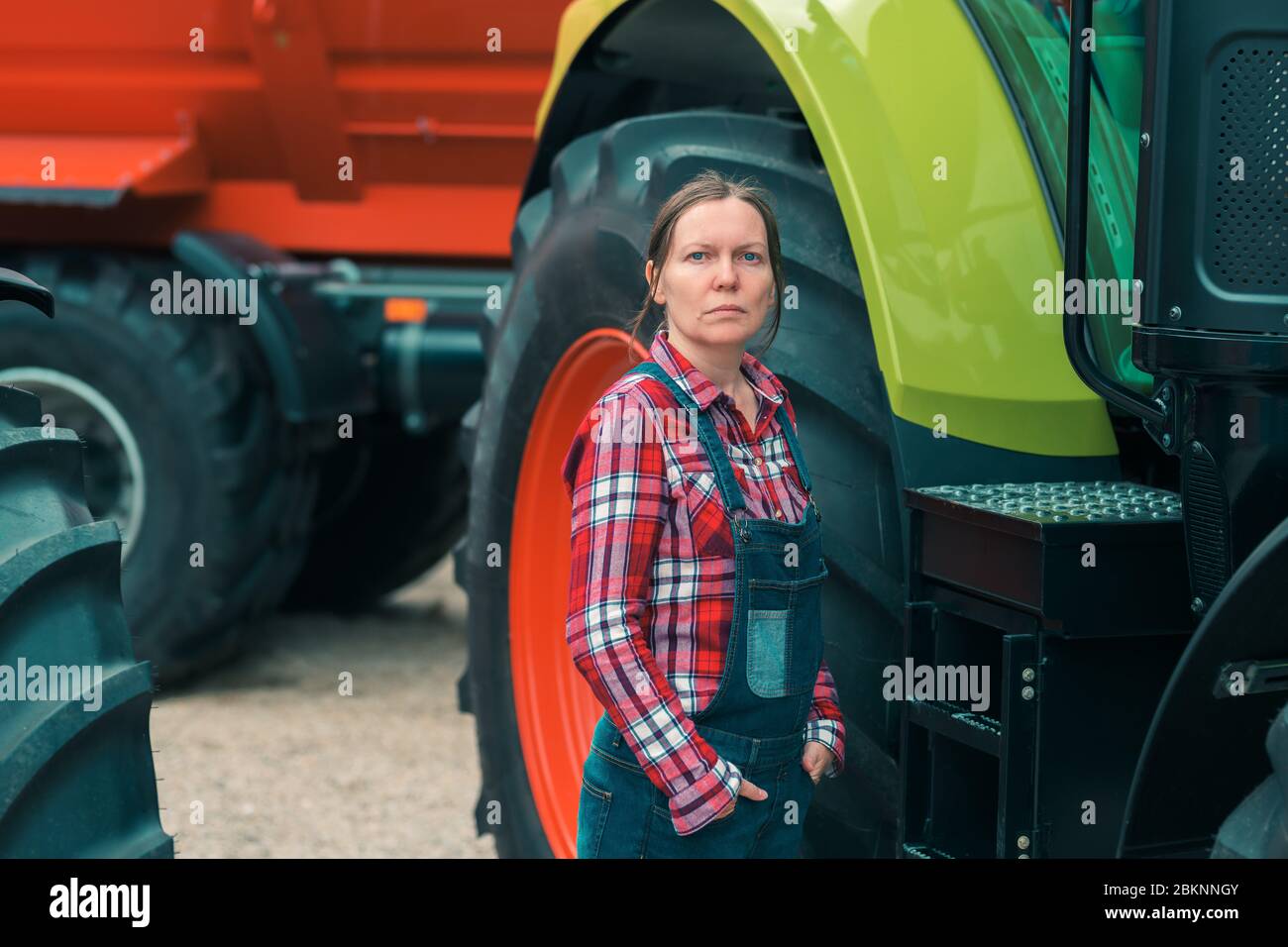 Female farmer and tractor. Woman doing men's job concept. Female farm worker posing in front of agricultural machinery. Stock Photo