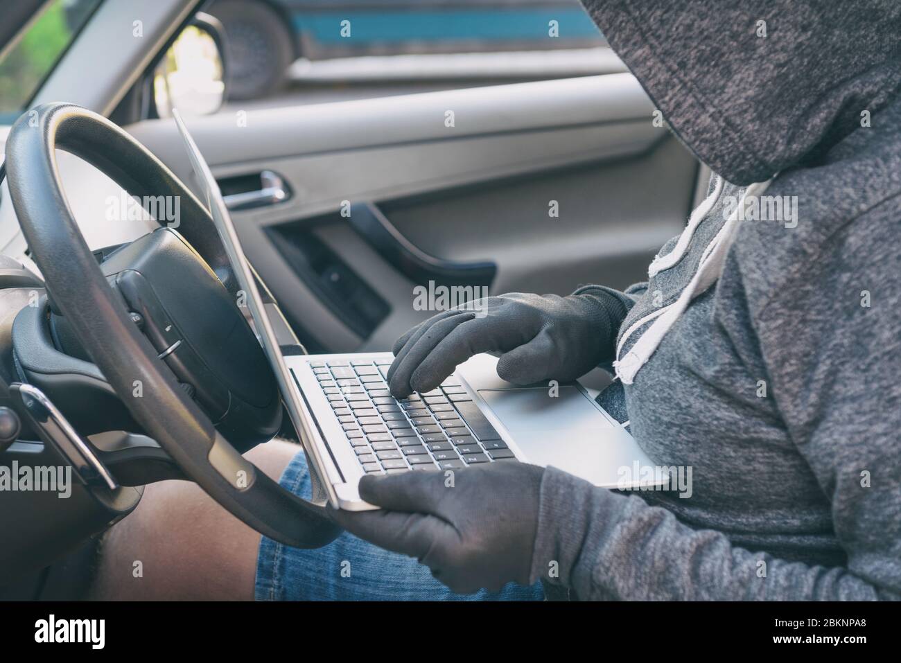 Hooded thief tries to break the car's security systems with laptop