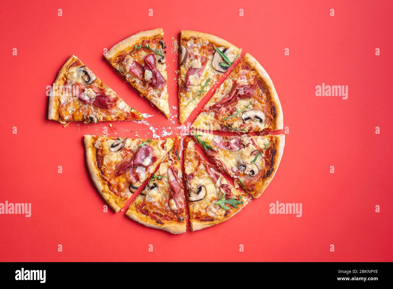 Pizza prosciutto sliced in eight on a red table. Homemade delicious