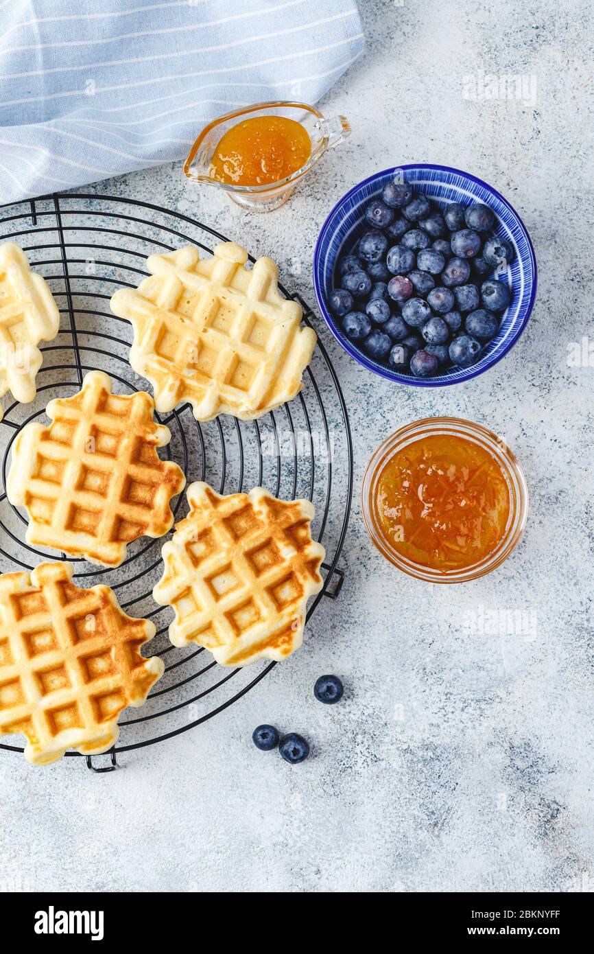 Traditional belgian homemade waffles with blueberry, honey and orange jam on metal grid on light