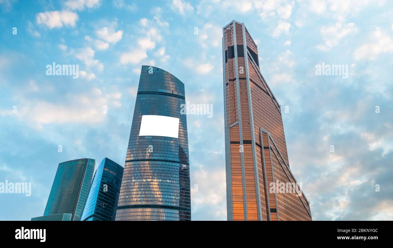 Blank white billboard or large advertising display on tall building, glass skyscraper and dramatic clouds against sunset sky. Mockup, isolated white Stock Photo