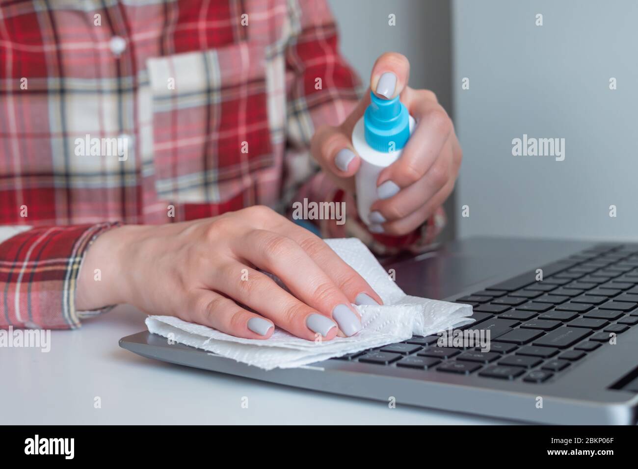 Woman hands spraying antiseptic, cleaning laptop keyboard with