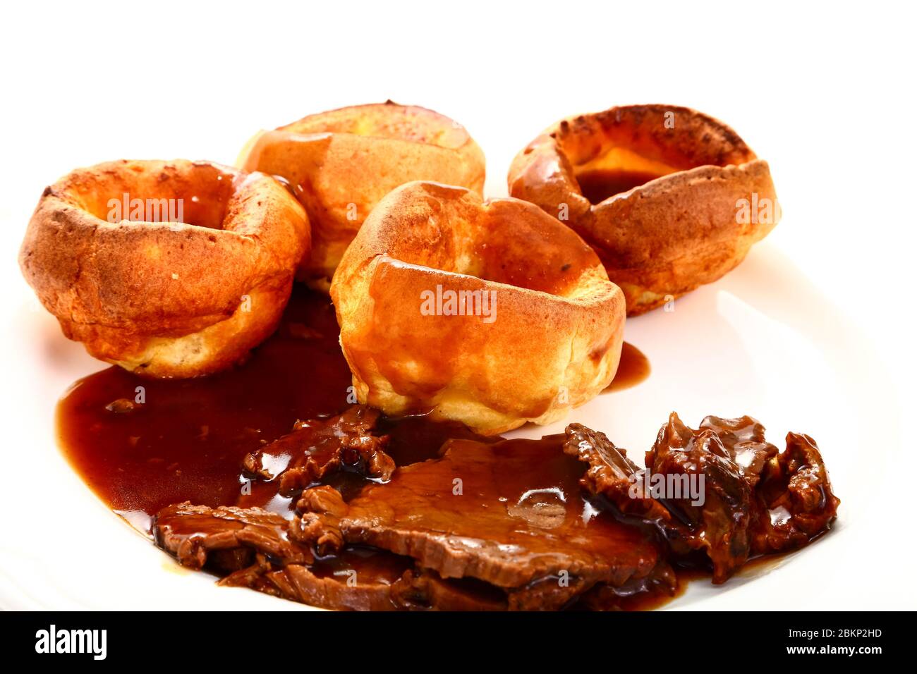 Traditional british meal of roast beef and yorkshire puddings with gravy on a white plate Stock Photo