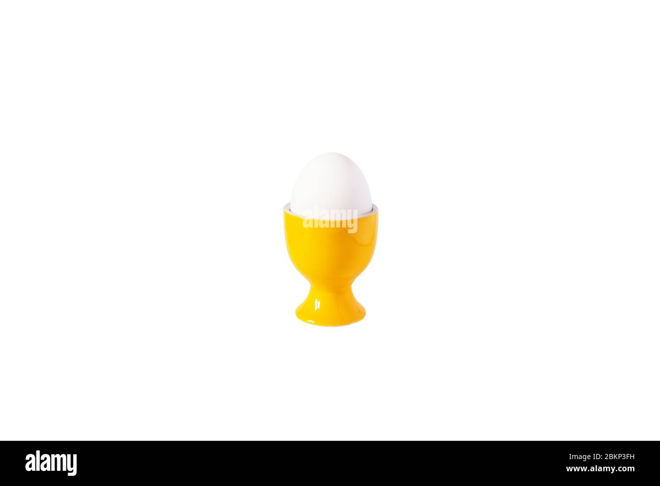 White egg standing on yellow egg cup, isolated on white background. Copy space. Stock Photo