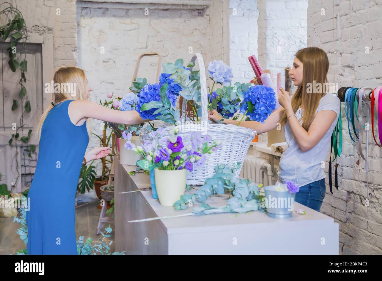 Two professional women floral artists, florists making large floral basket with flowers at workshop, flower shop. Floristry, handmade, wedding Stock Photo