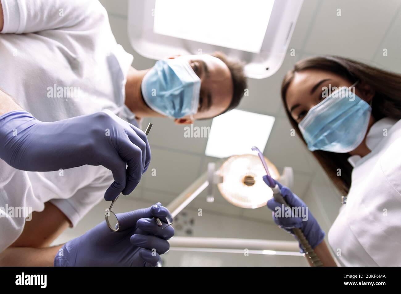 The dentist and assistant bent over the patient to examine the teeth, treat them or create a denture. A man and a woman are holding examination instruments, a saliva tube and looking at the patient. Stock Photo