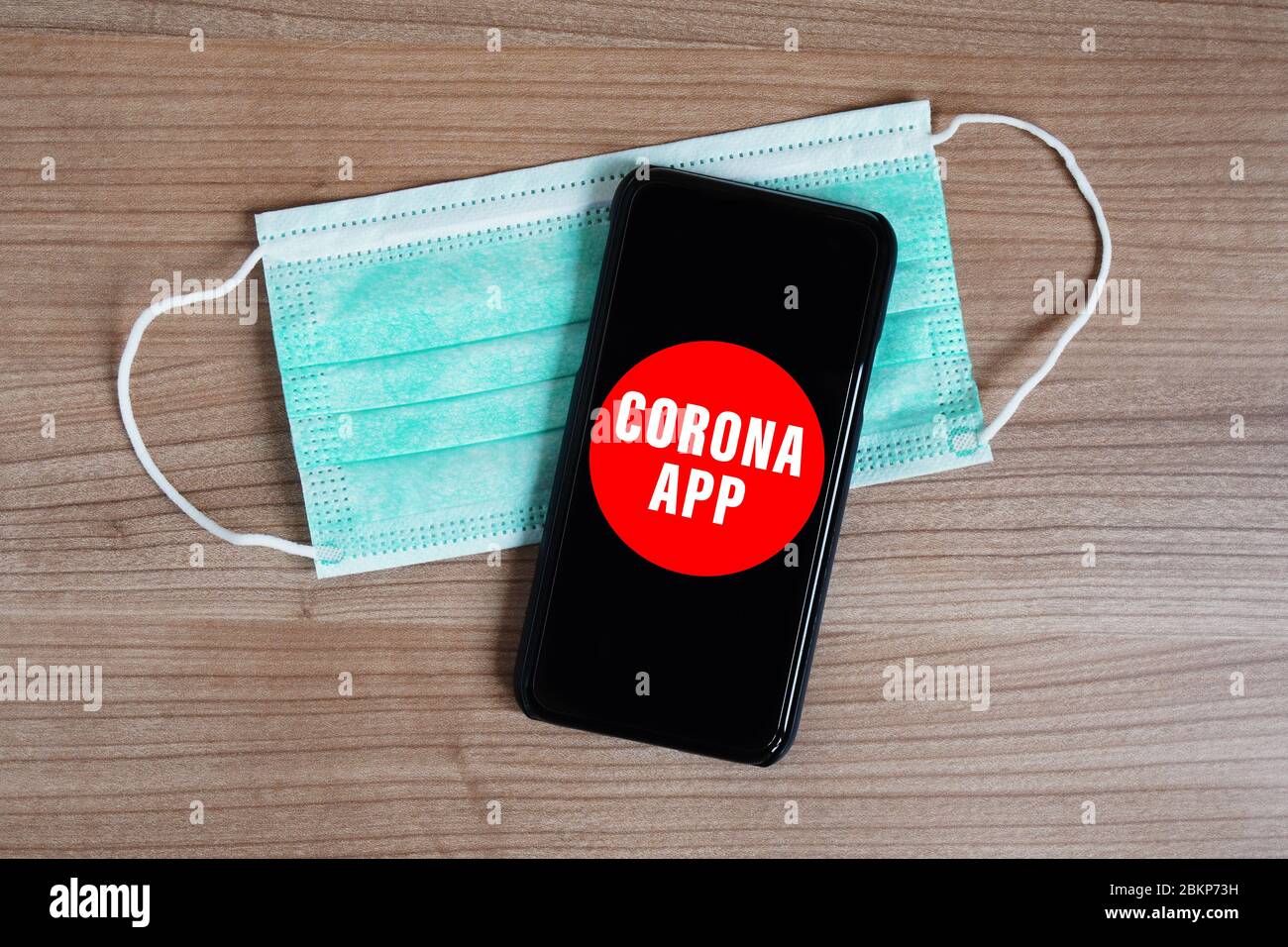 mock-up corona app on smartphone or mobile and face mask on desk - fictive coronavirus covid-19 mobile tracking software to control virus spread Stock Photo