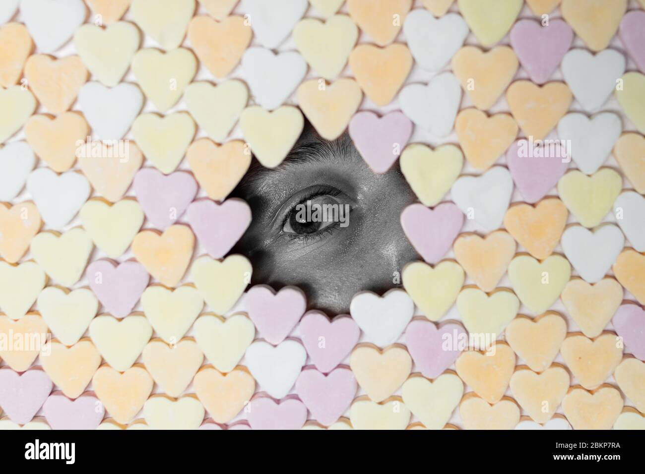 Girl looking through hole in wall of heart-shaped sweets. Black and white face. Royalty free stock photo. Stock Photo