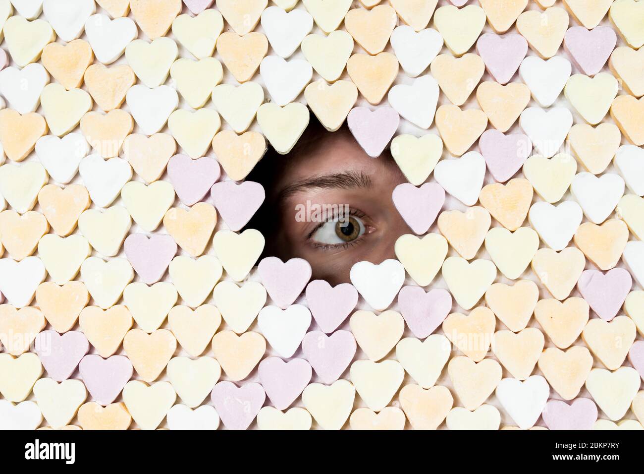 Girl peaking through hole in wall of heart-shaped sweets. Royalty free stock photo. Stock Photo
