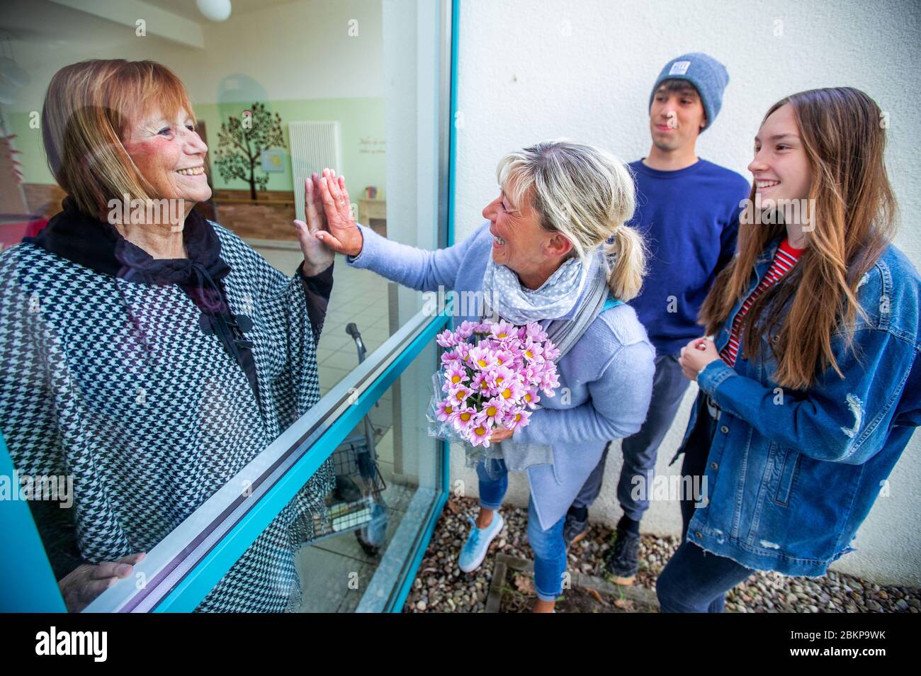 Schwerin, Germany. 05th May, 2020. Anne-Katrin Lampe, with a bouquet of flowers and her children Marty and Juliane, visits her 80-year-old mother Bärbel Prütz at the AWO senior citizens' home in Schelfwerder, which is closed to visitors because of the corona crisis, and holds her hand against a window pane. The family regularly visits the resident of the nursing home and waves to each other through the large window on the ground floor. Credit: Jens Büttner/dpa-Zentralbild/dpa/Alamy Live News Stock Photo