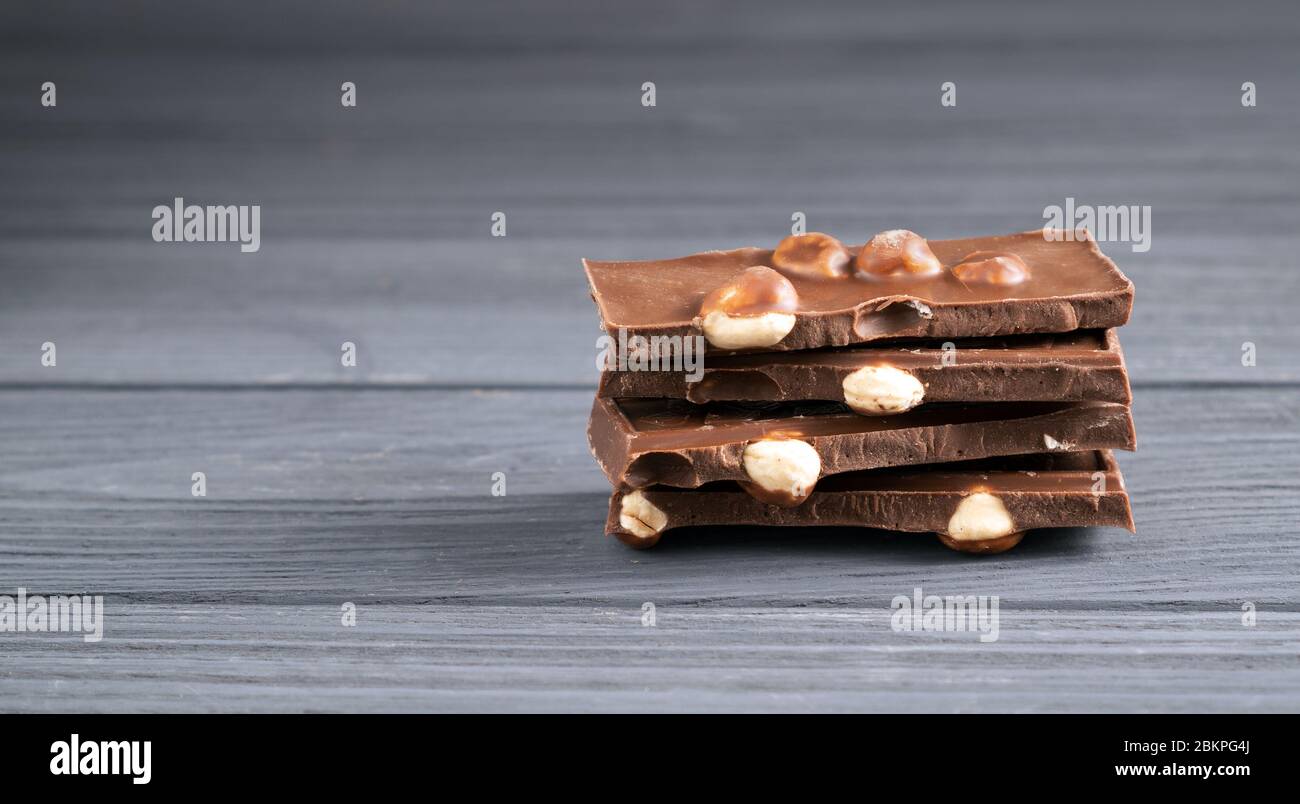 Stack of milk chocolate pieces with nuts on gray wooden table. Pile of chocolate bars Chocolate pieces with big hazelnut Stock Photo