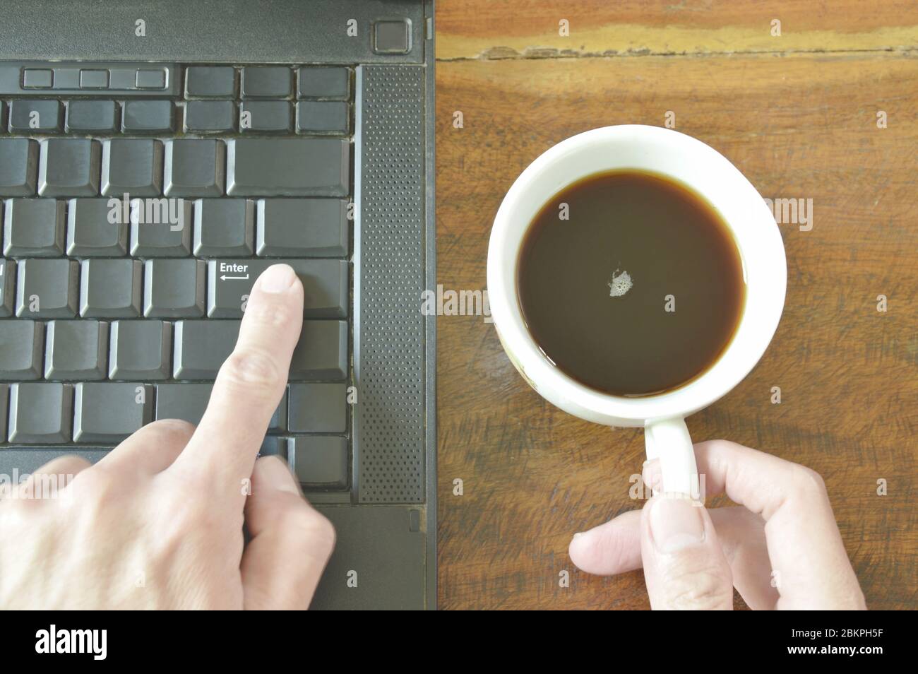 finger pushing enter button on computer notebook while holding coffee cup Stock Photo