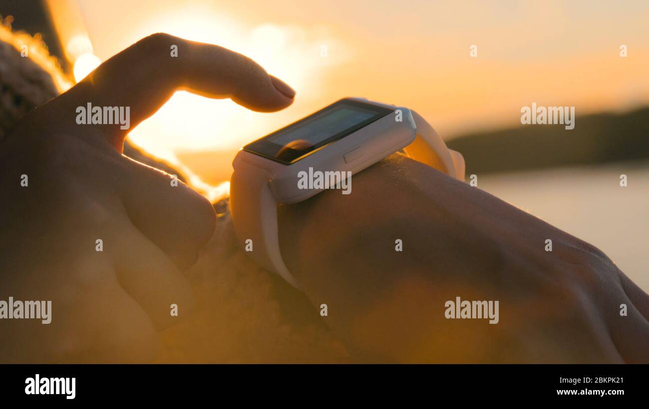 Woman using wearable smartwatch computer device on deck of cruise ship at sunset. Sunset light, sun lens flares, golden hour. Relax, nature and Stock Photo