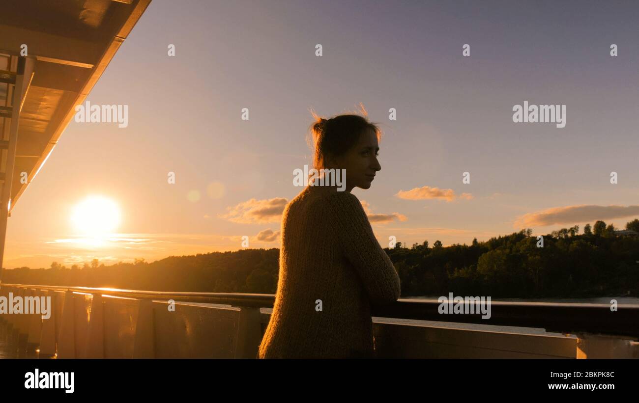 Woman standing on deck of cruise ship and looking at landscape. Sunset ...