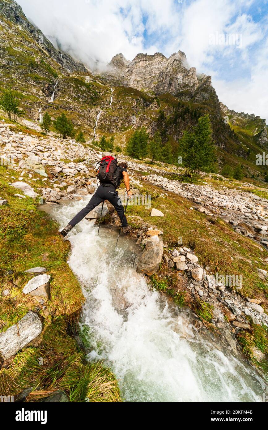 Hiker crossing stream in Val Buscagna Parco Naturale Veglia Devero Piemonte Italy Stock Photo