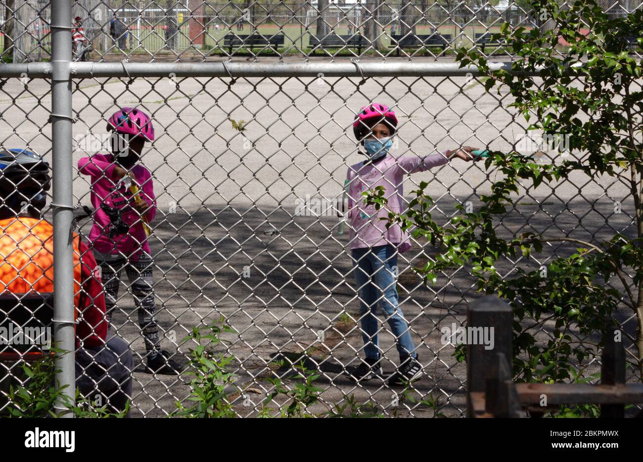 a girl playing with a face mask on and other children behind a chain link fence in Van Cortlandt Park due to the coronavirus or covid-19 pandemic Stock Photo