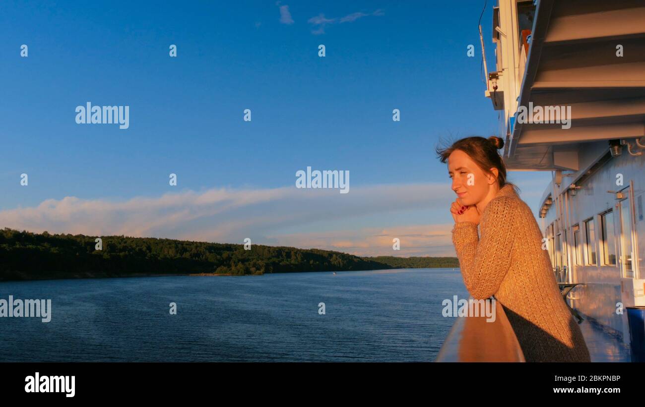 Woman standing on deck of cruise ship and looking at landscape. Sunset ...