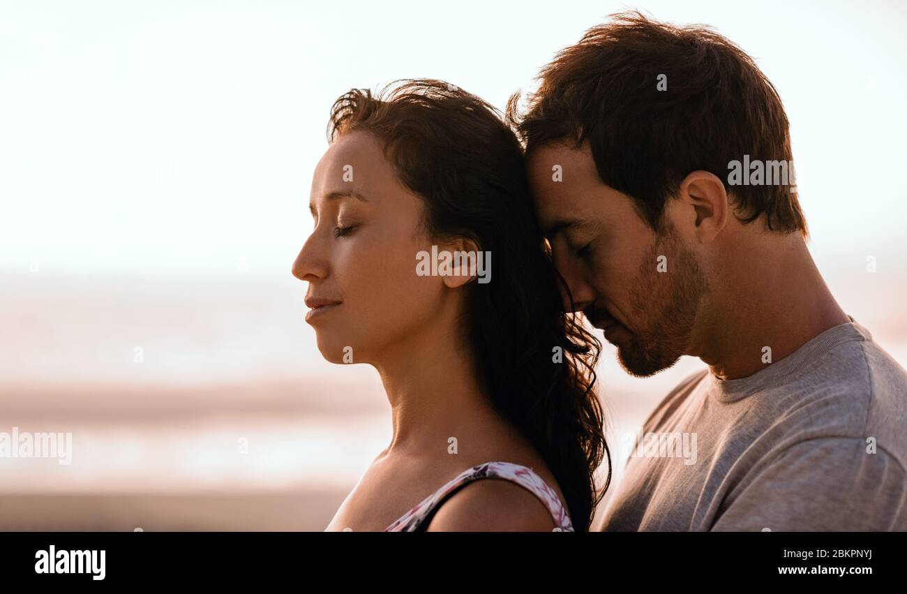 Young couple standing close together on a beach at dusk Stock Photo