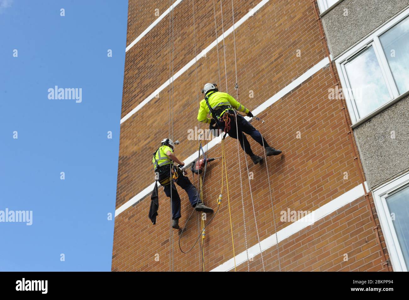 Men working at height on ropes. Industrial rope access workers on the wall of a high residential block of flats. They are wearing professional safety Stock Photo