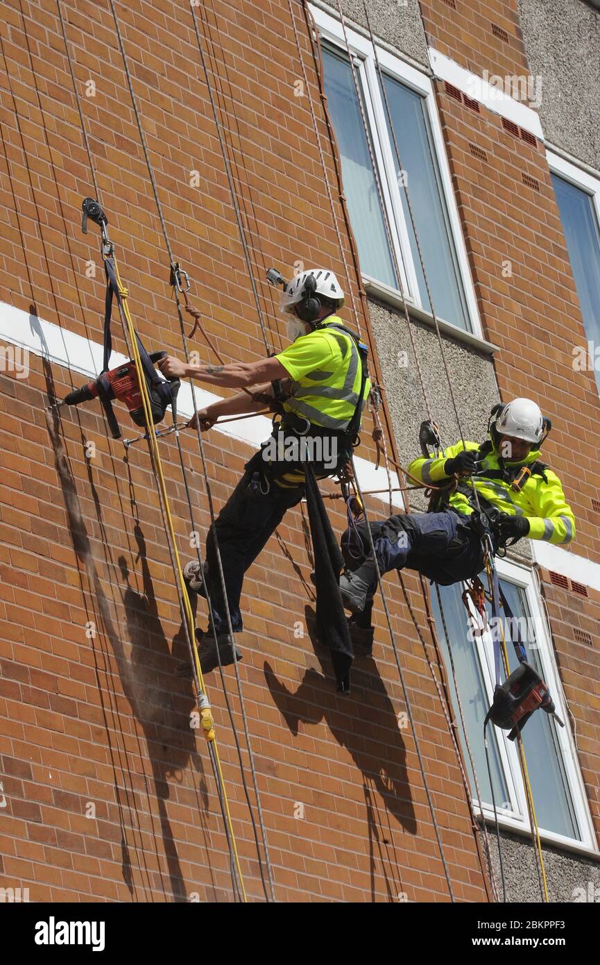 Men working at height on ropes. Industrial rope access workers on the wall of a high residential block of flats. They are wearing professional safety Stock Photo