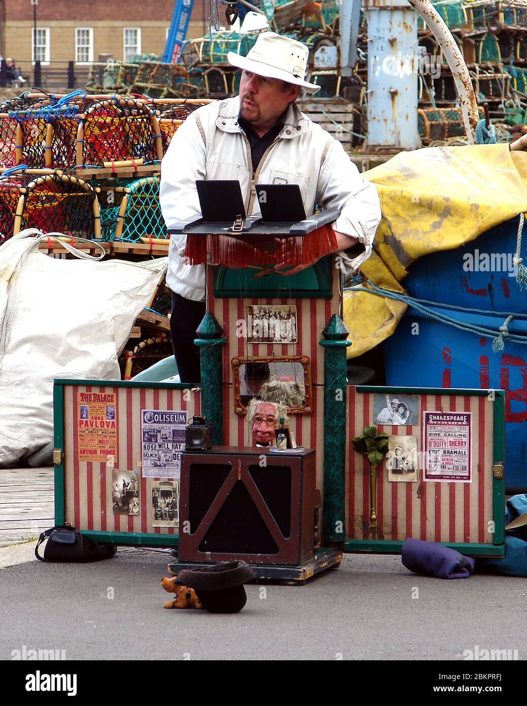 2017 - WHISTLE WHILE YOU WORK -  A busker in Whitby , North Yorkshire,UK, with an unusual puppet theatre show. Traditional Yorkshire crab/lobster pots are stacked on the quayside behind him. His 'theatre'  has lots of old miniature theatre and cinema posters  with stars names plus photographs of music hall stars. Stock Photo