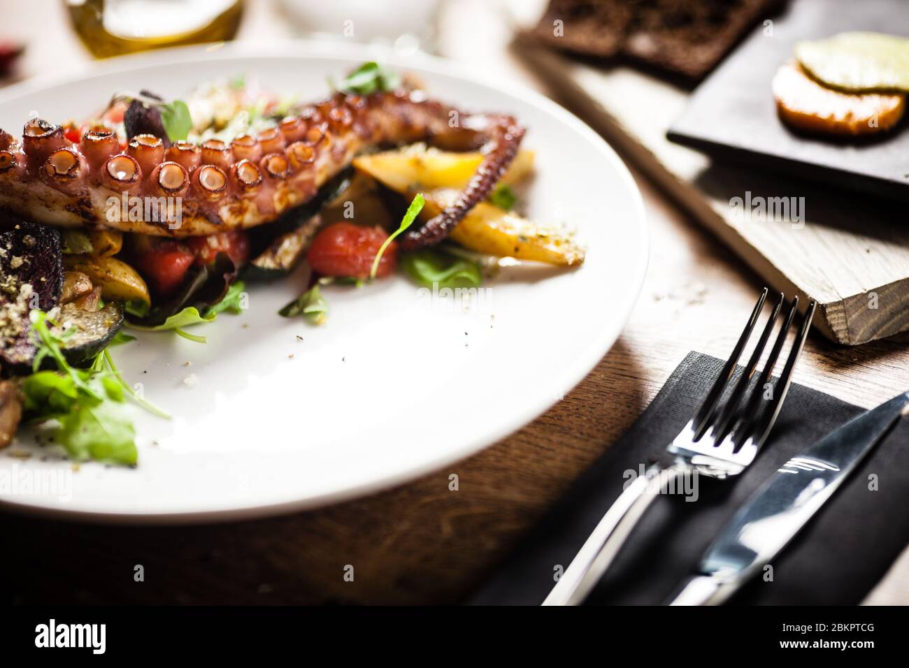 Warm octopus salad with stir fried vegetables and aji sauce on white plate. Delicious healthy mediterranean traditional seafood closeup served on a Stock Photo