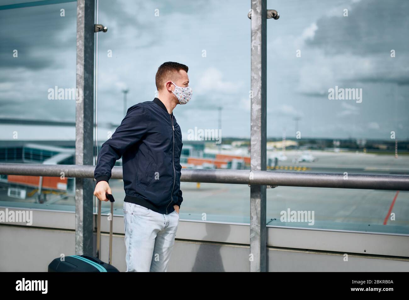Man wearing face mask and waiting for flight at airport. Themes traveling during pandemic, internet connection and personal protection. Stock Photo