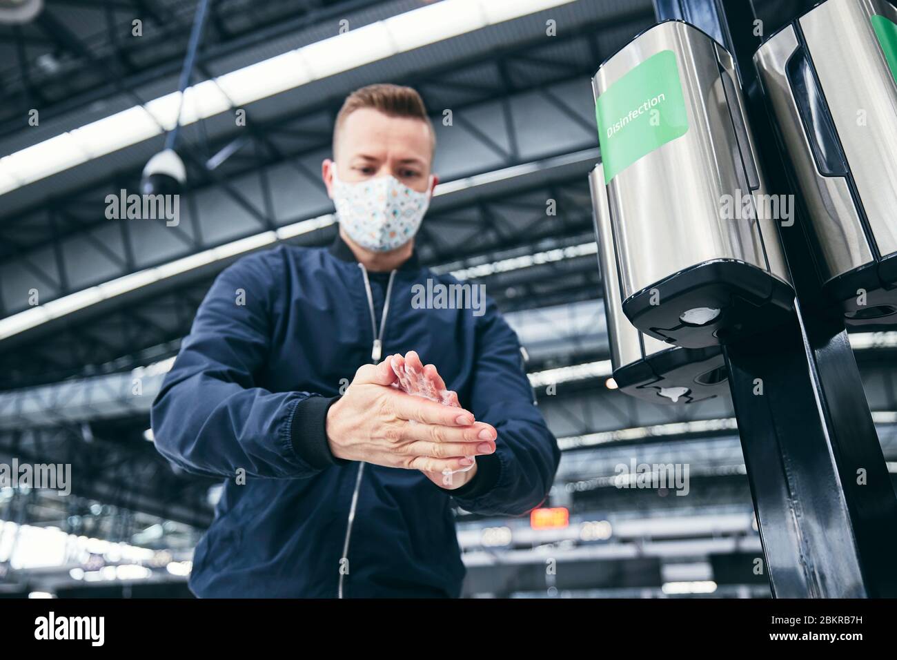 Man wearing face mask and using hand sanitizer at airport. Themes traveling during pandemic, hygiene and personal protection. Stock Photo