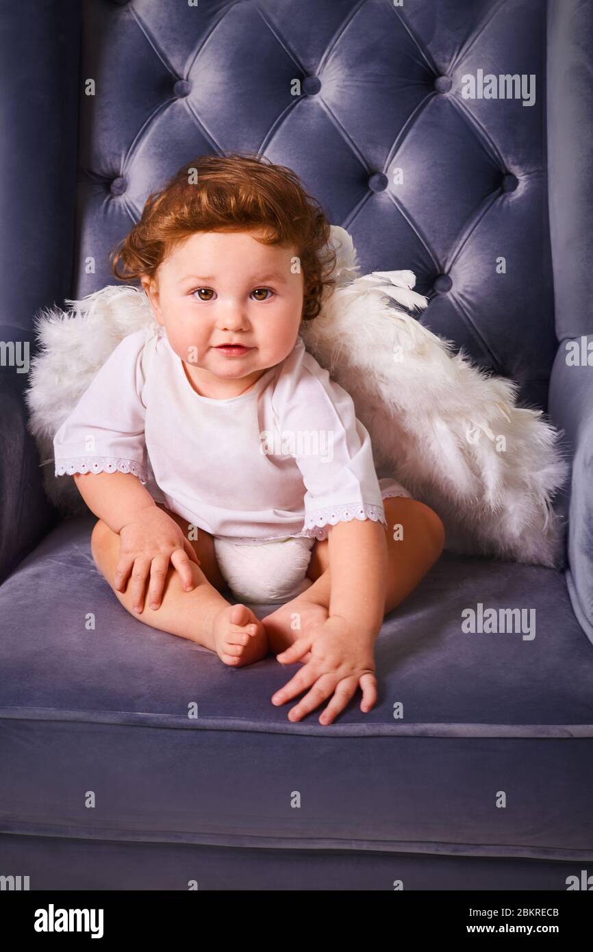 Little boy 1 year old like angel surprised and sit on luxurious