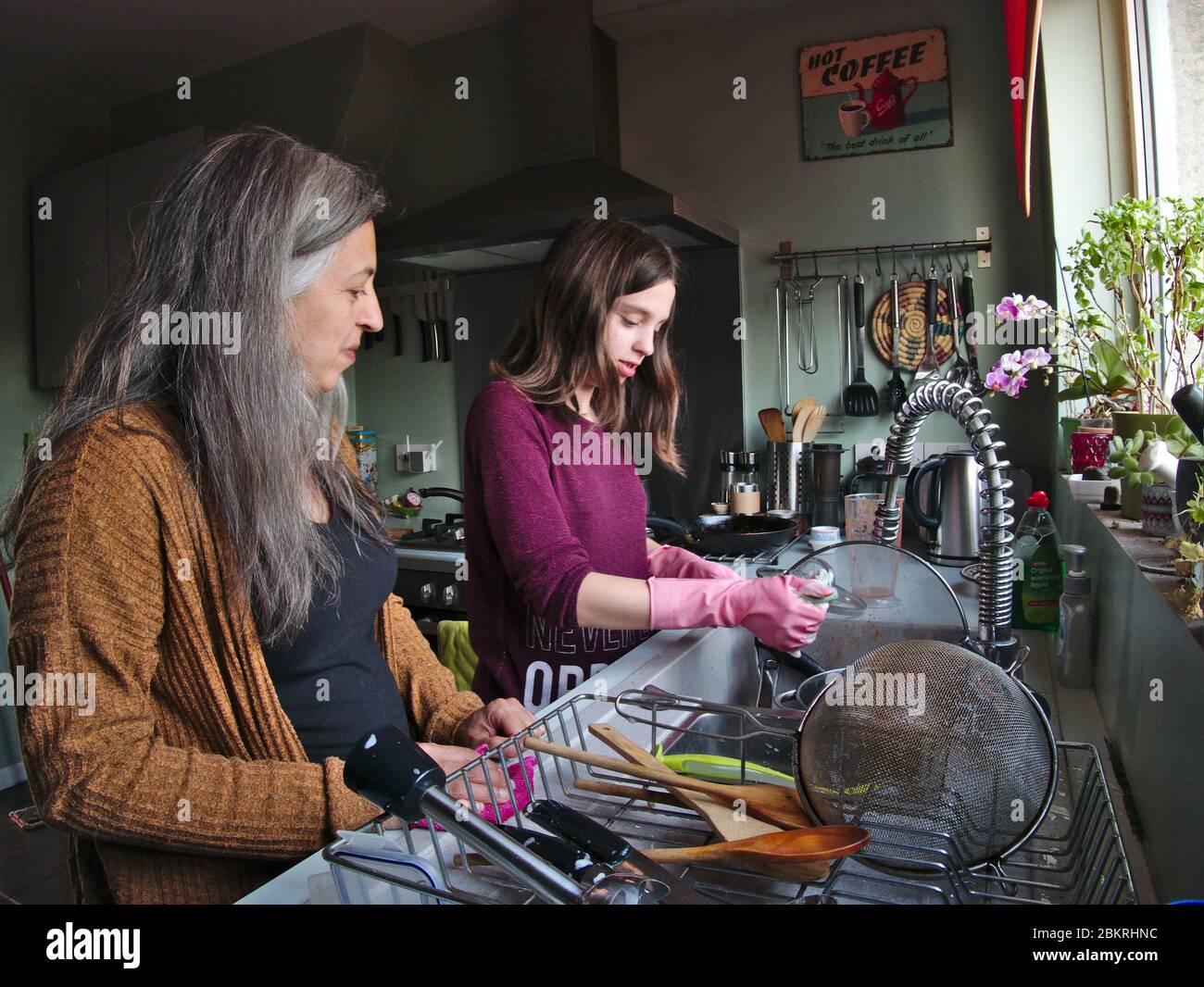 Thirteen year old girl doing washing up at home watched by her Mother. Stock Photo