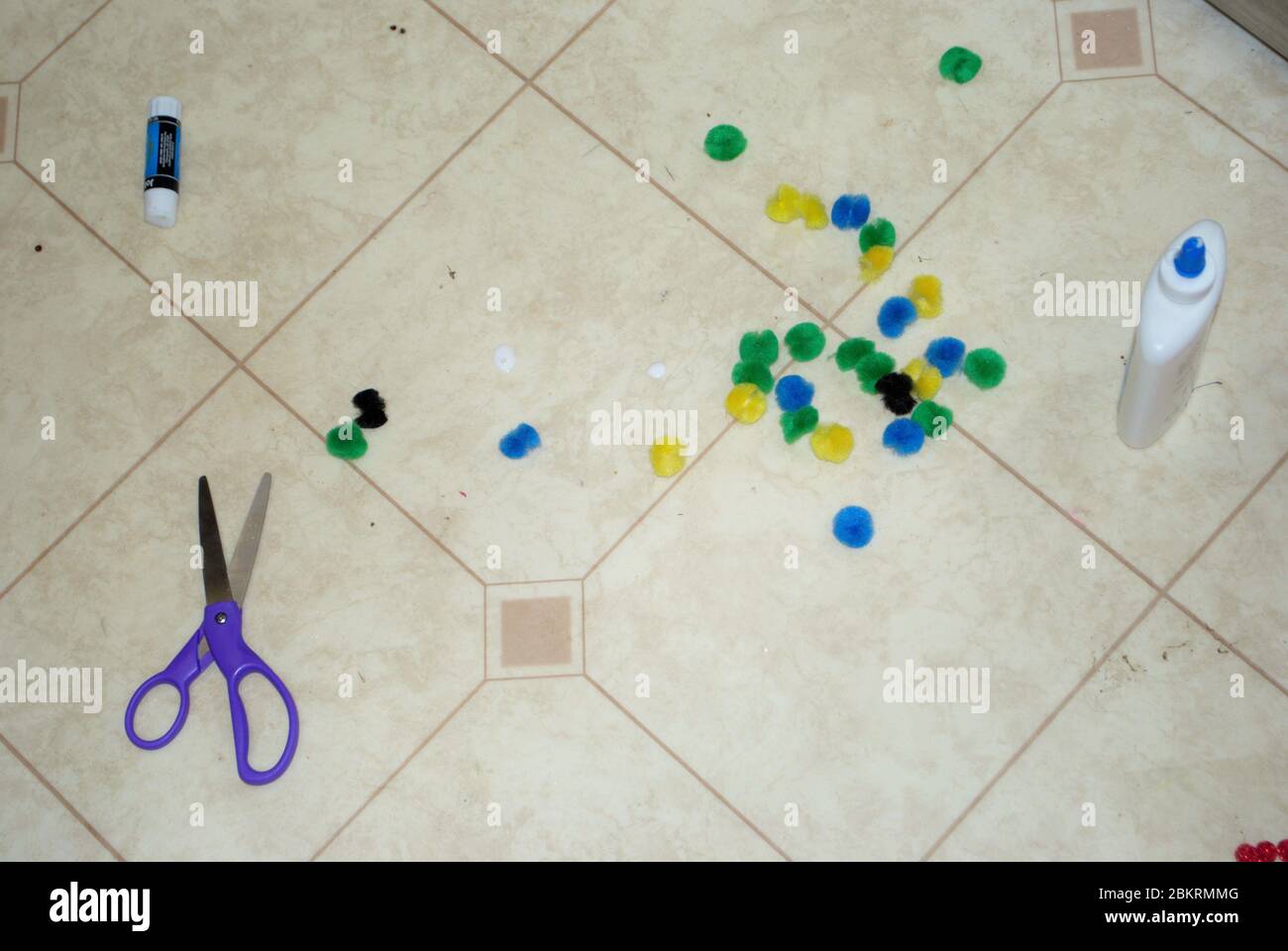 Multi colored cotton balls glue and scissors on a linoleum floor during