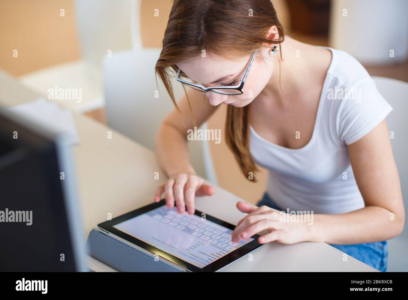 Smiling female student/ businesswoman using her tablet computer and a desktop computer, staying up to date, working, looking at the camera. Stock Photo