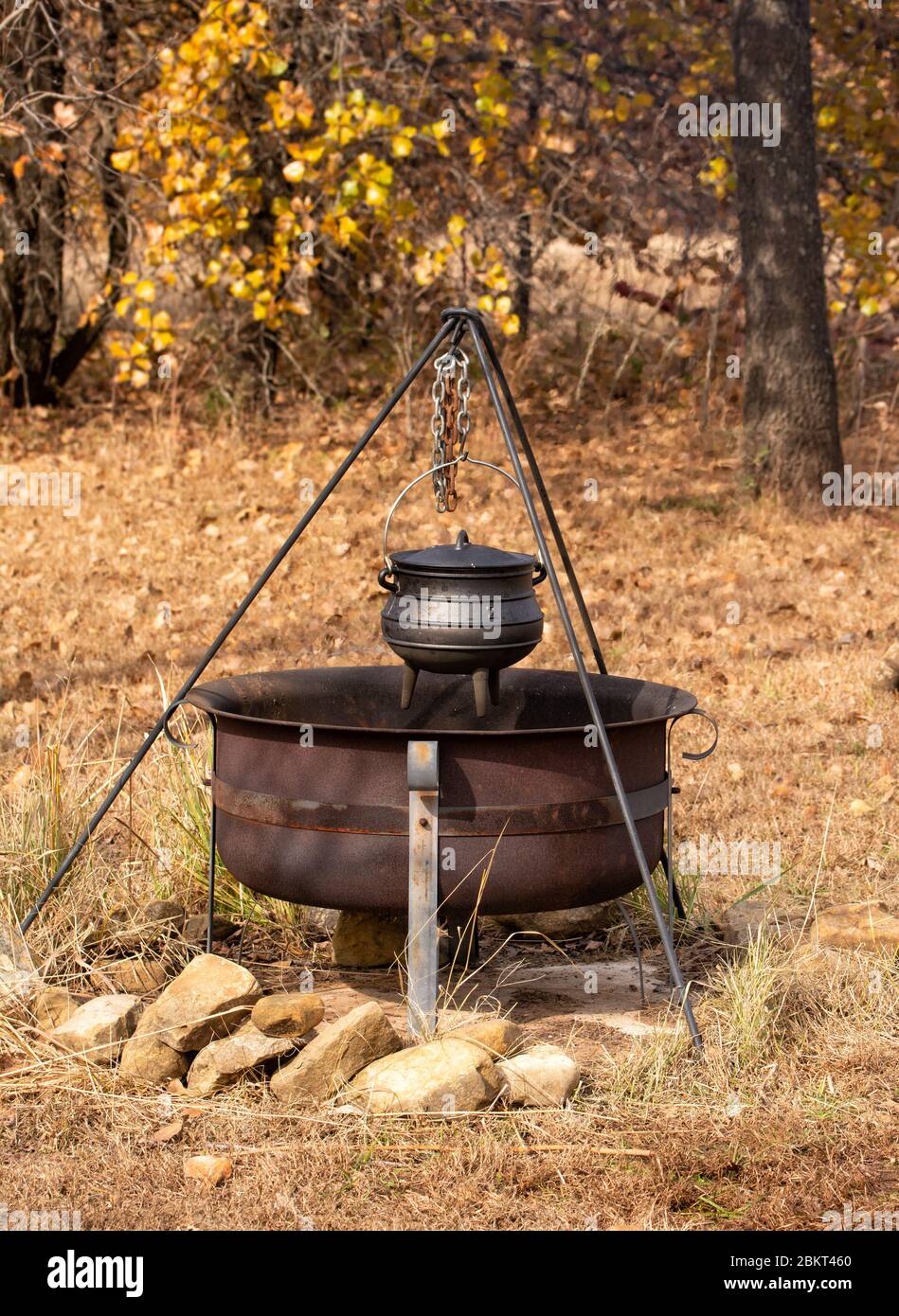 Stew cooking in a cast iron potjie suspended over open fire in a fire pit outdoors; with fall color background Stock Photo