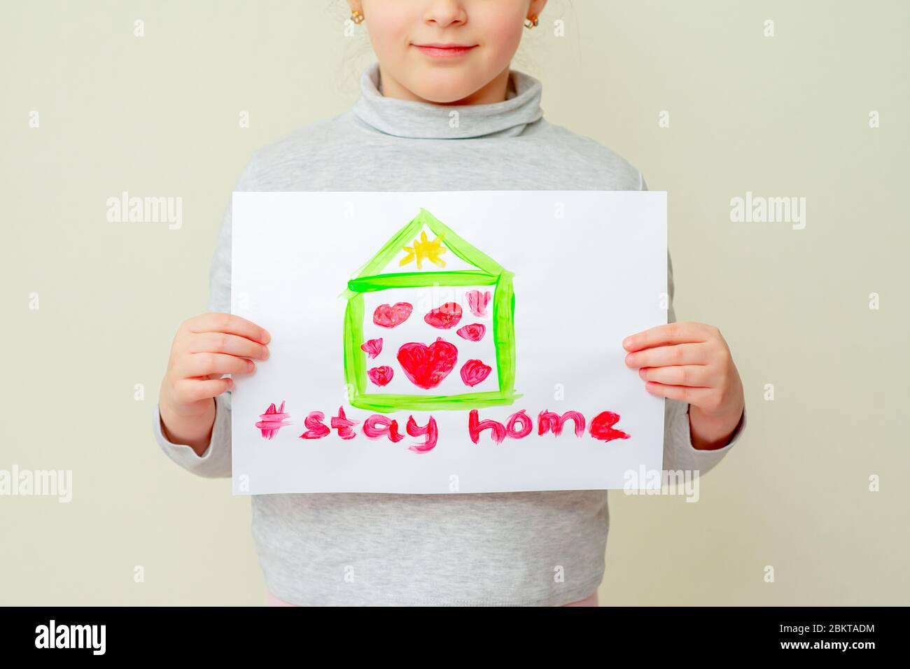 Child is holding a picture of house with hearts and words Stay Home on yellow background. Stay Home concept. Stock Photo