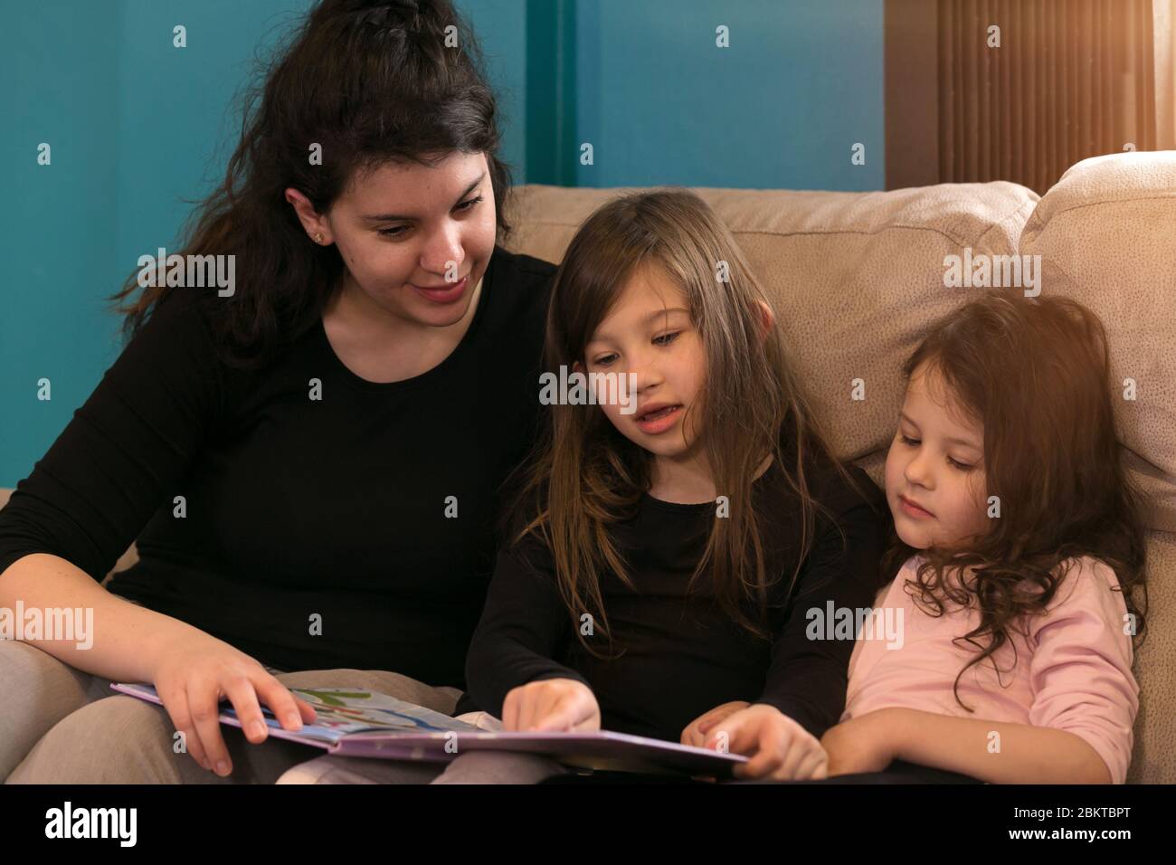 Two young children reading stories with their mother on the couch Stock Photo
