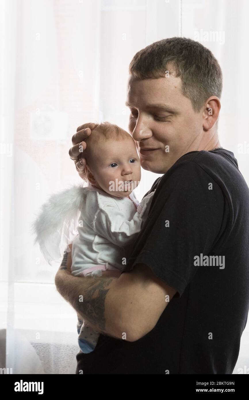 A young man gently holds a baby with angel wings in his arms. Happy father and daughter Stock Photo