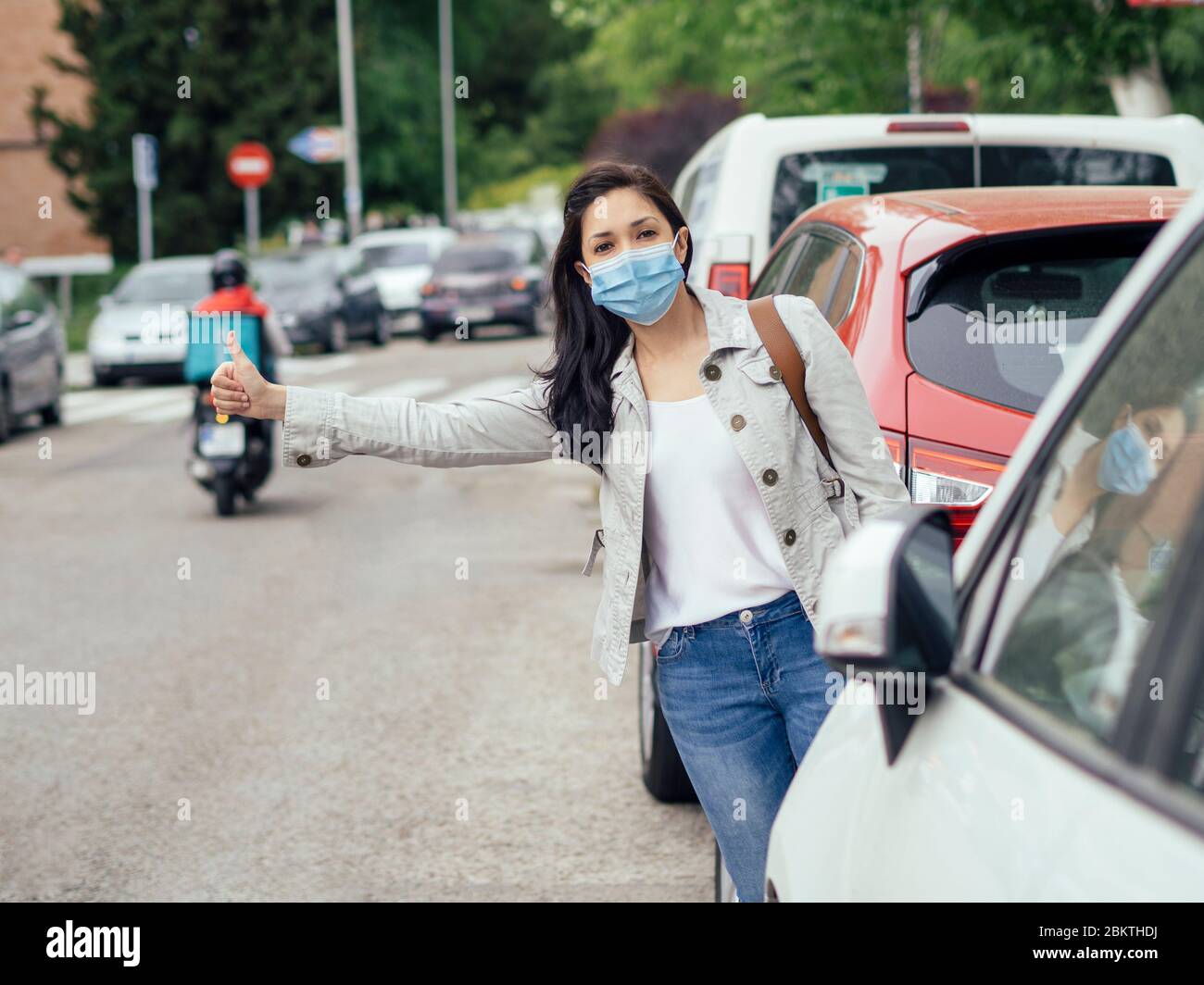 Woman hitchhiking. She is wearing a protective mask for the prevention of a virus. Coronavirus concept. Stock Photo