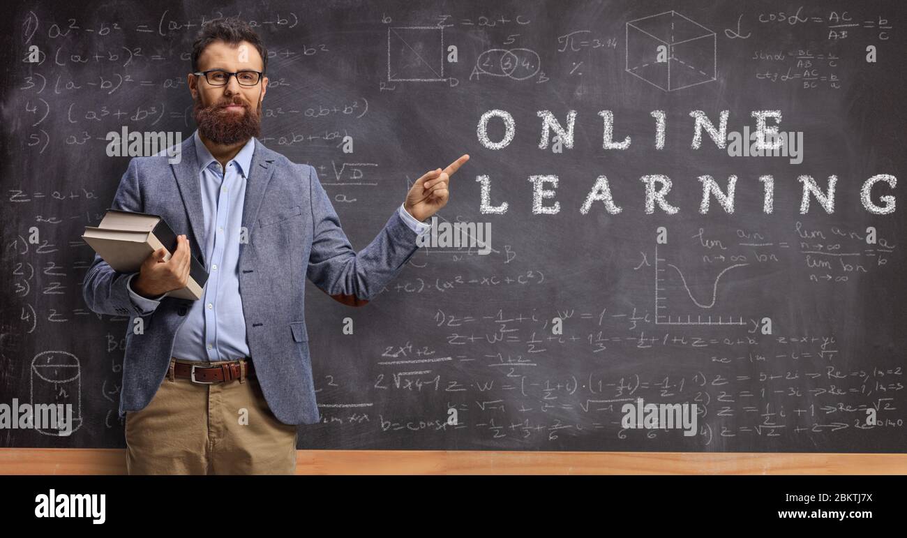 Bearded male teacher holding books and pointing at a blackboard with text online learning Stock Photo