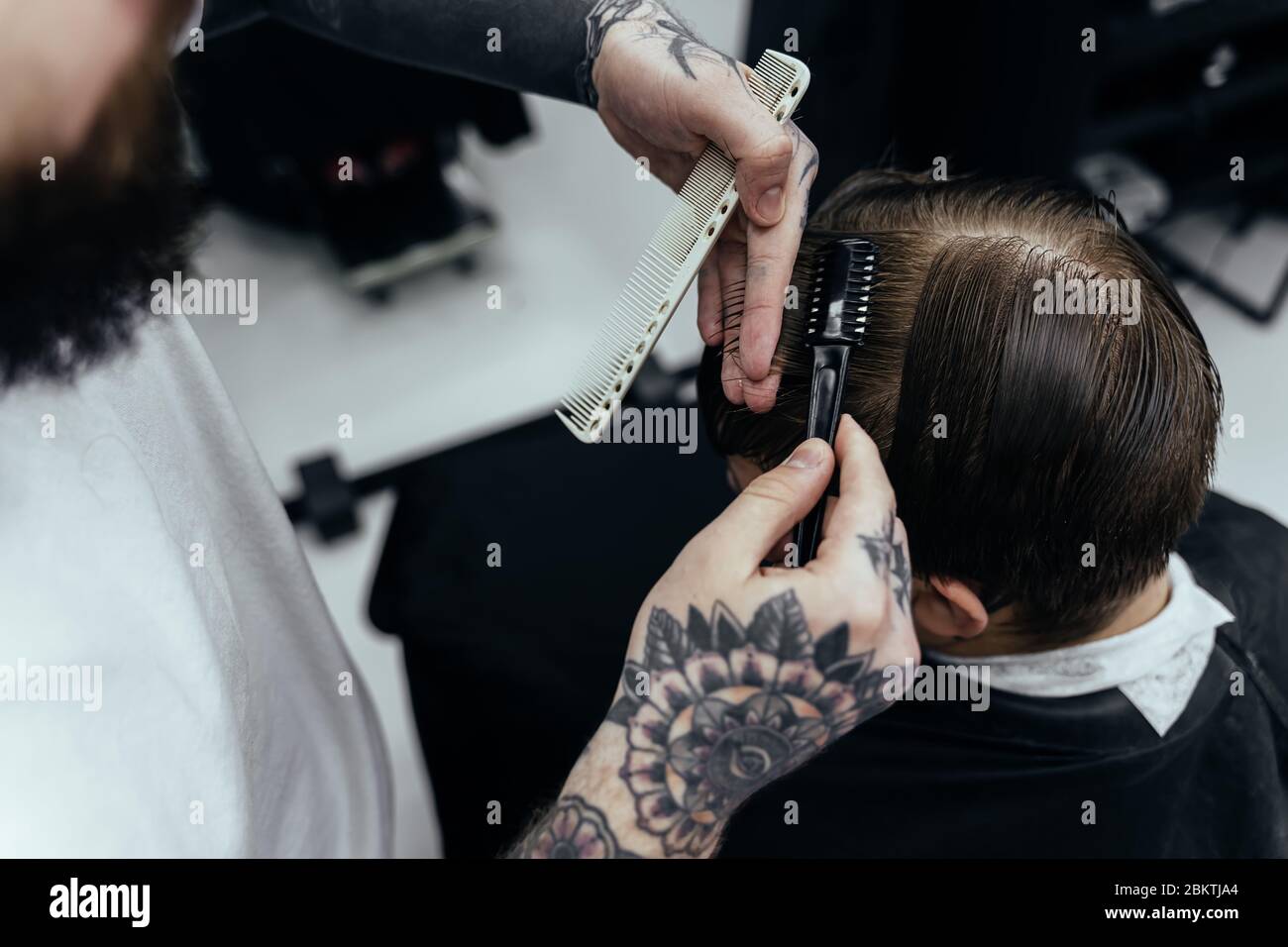 Professional tattooed barber using cutthroat razor cutting hair. Attractive male is getting a modern haircut in barber shop. Close up. Stock Photo