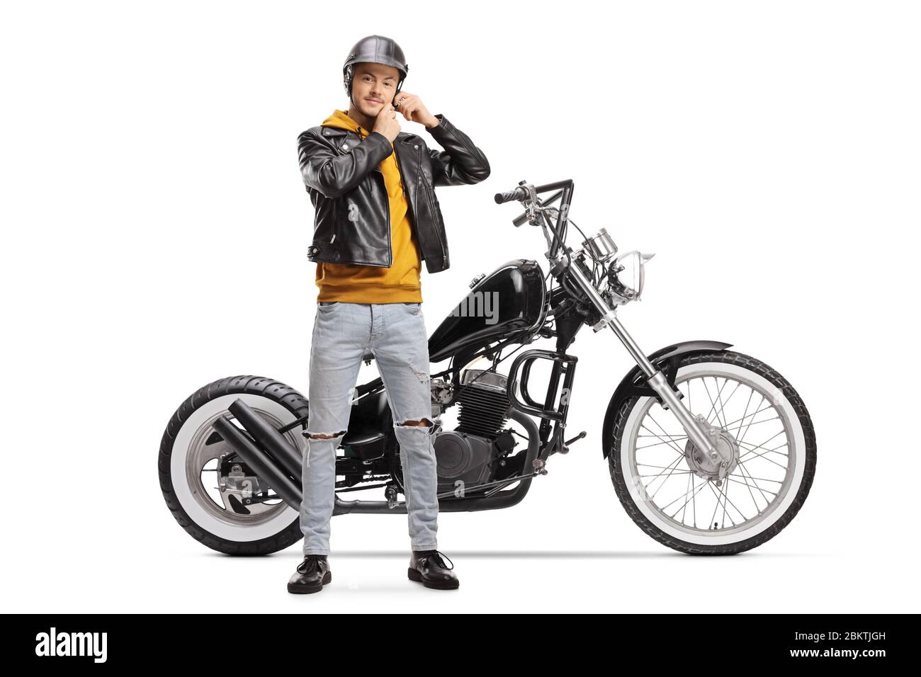 Young biker taking off helmet and standing next to chopper motorbike isolated on white background Stock Photo