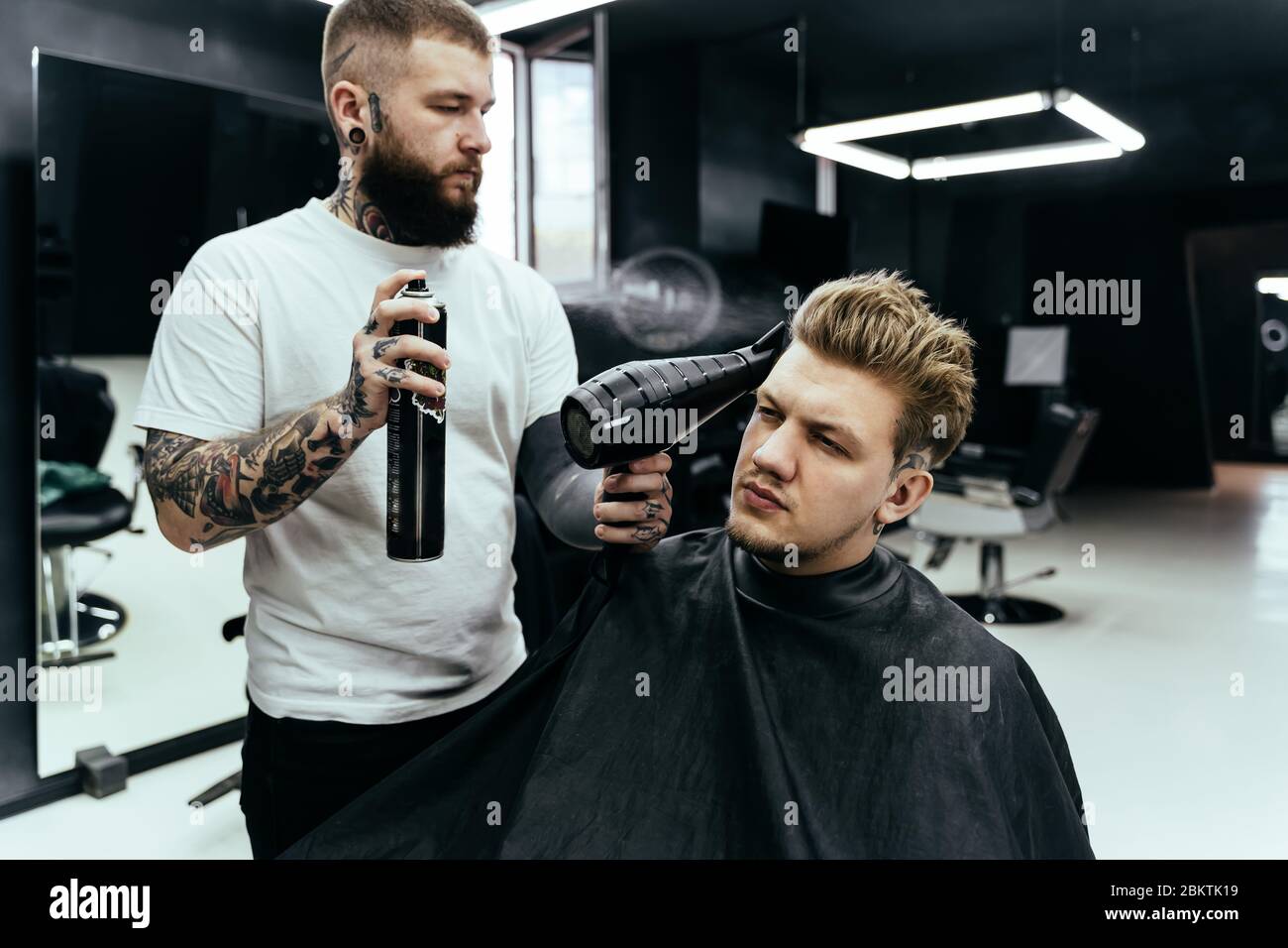 Barber makes hair styling with hair spray after haircut at the barber shop.  Young handsome Caucasian man getting a haircut in a modern hairsalon Stock  Photo - Alamy