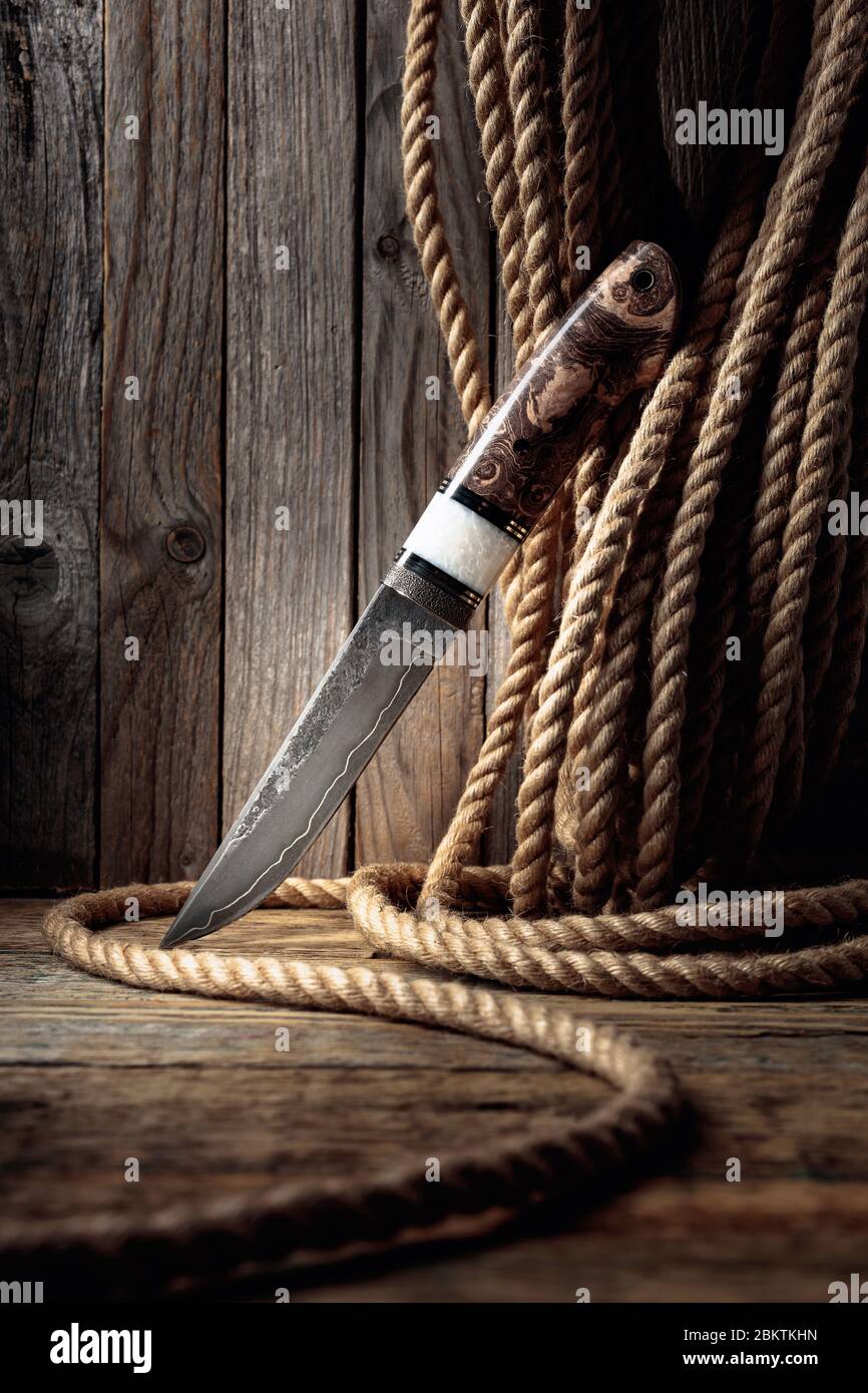 Hunter hand made knife and hemp rope on wooden background. The surface