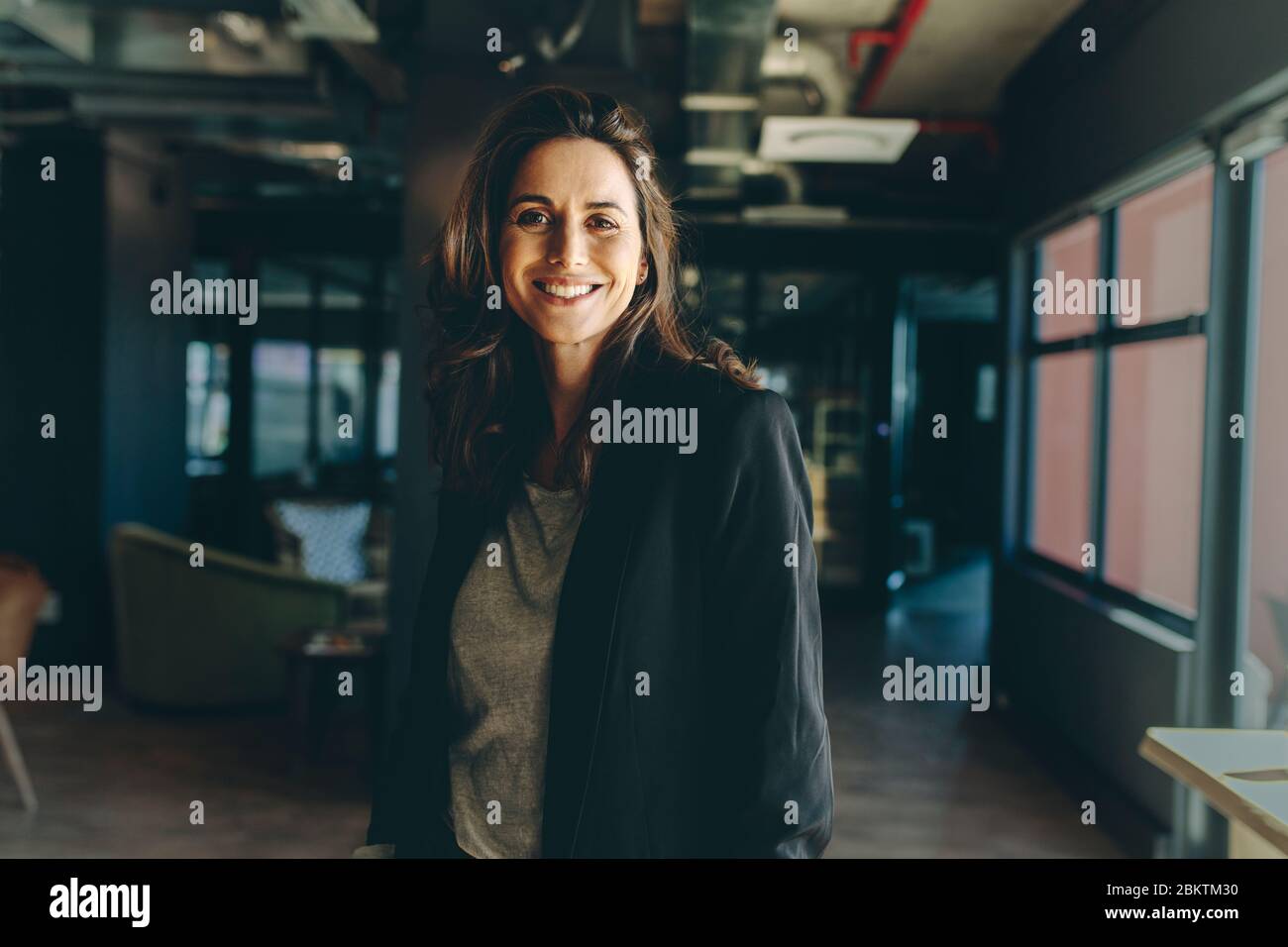 Smiling female executive standing in office. Woman in formal business attire looking at camera and smiling. Stock Photo