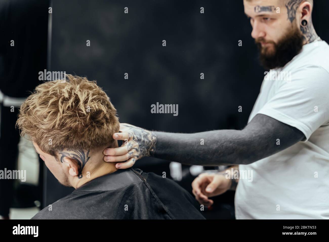 Barber makes hair styling with hair gel and comb after haircut at the barber shop. Young handsome Caucasian man getting a haircut in a modern Stock Photo