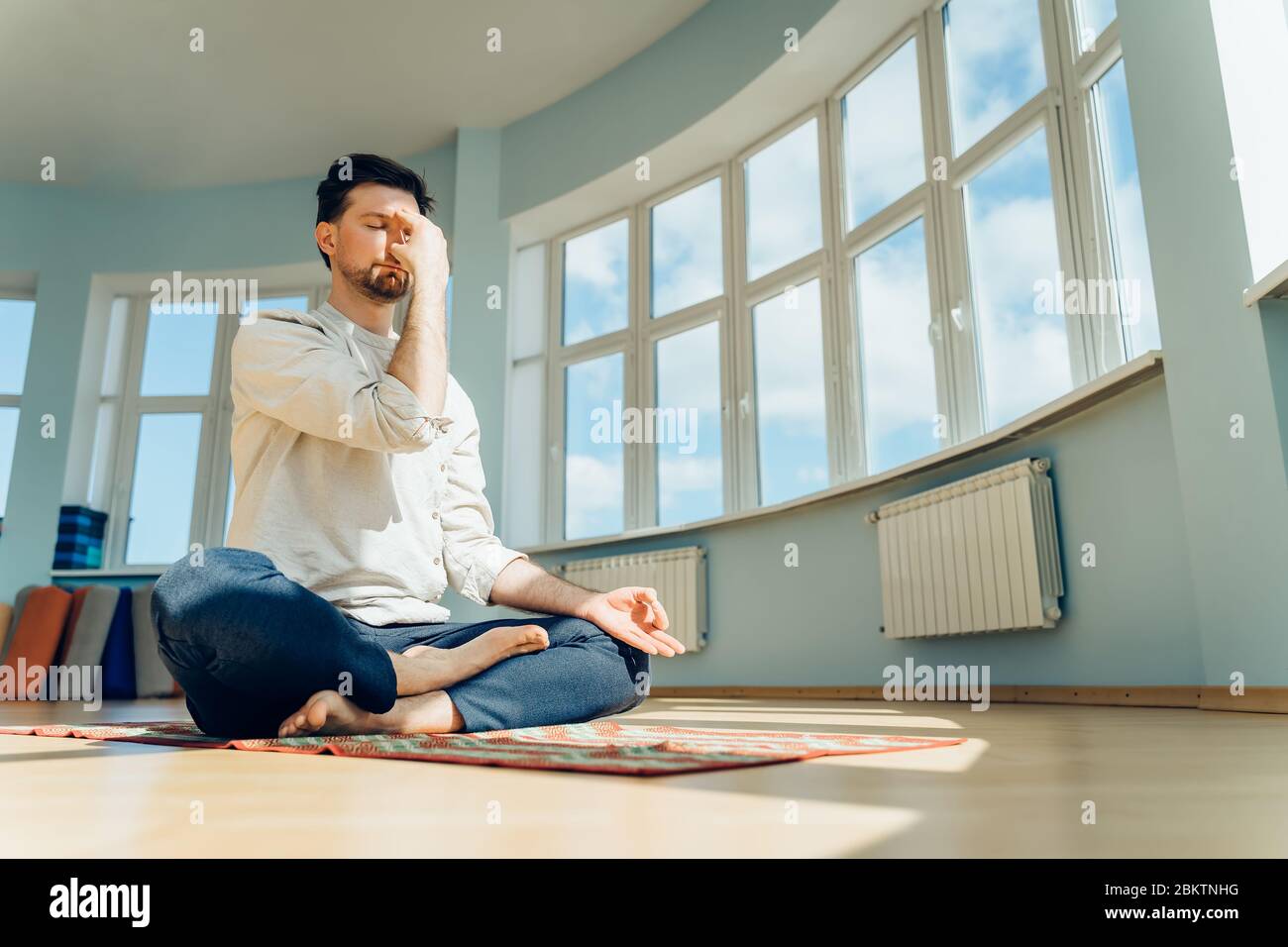 Man practice yoga. Young attractive male doing breathing exercises. Guy meditating at home along during the pandemic. Relaxation and resting concept Stock Photo