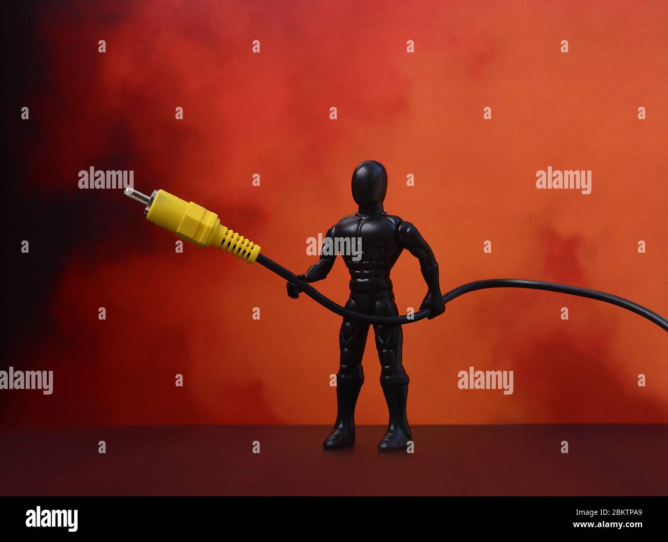 USB cable. USB cable, in the hands of Superman. Red background. USB cable on a red background. Plastic man Stock Photo