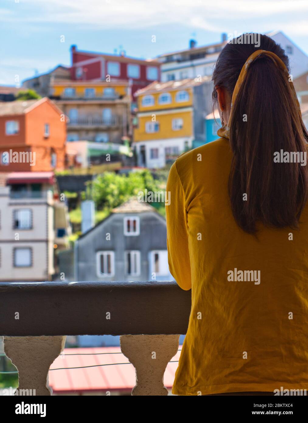 Young woman clapping her hands on the balcony to showi gratitude to all healthcare workers during the coronavirus outbreak. Lots of colorful houses. Stock Photo
