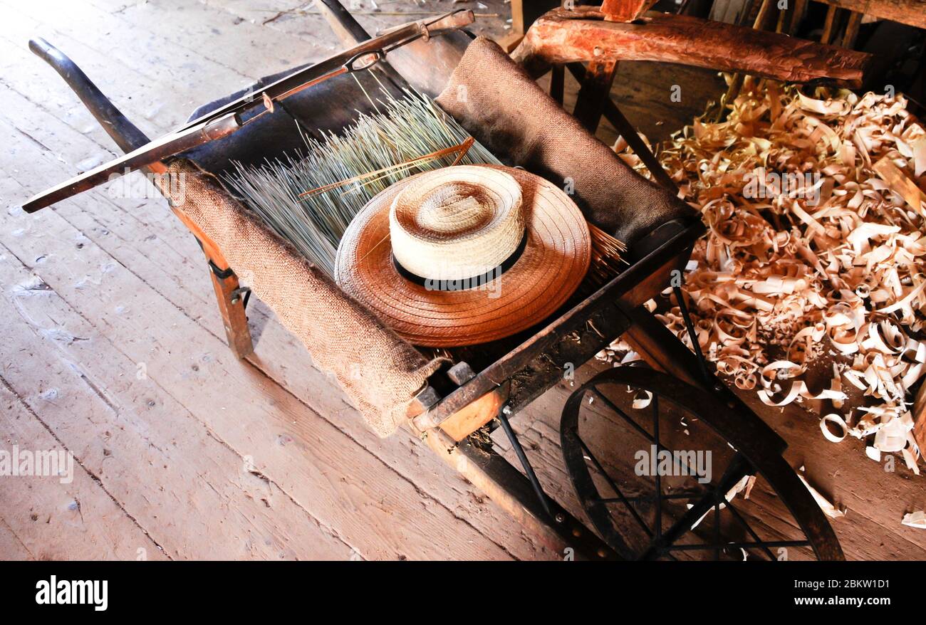 An old wooden wheelbarrow with straw hat and saw. Stock Photo